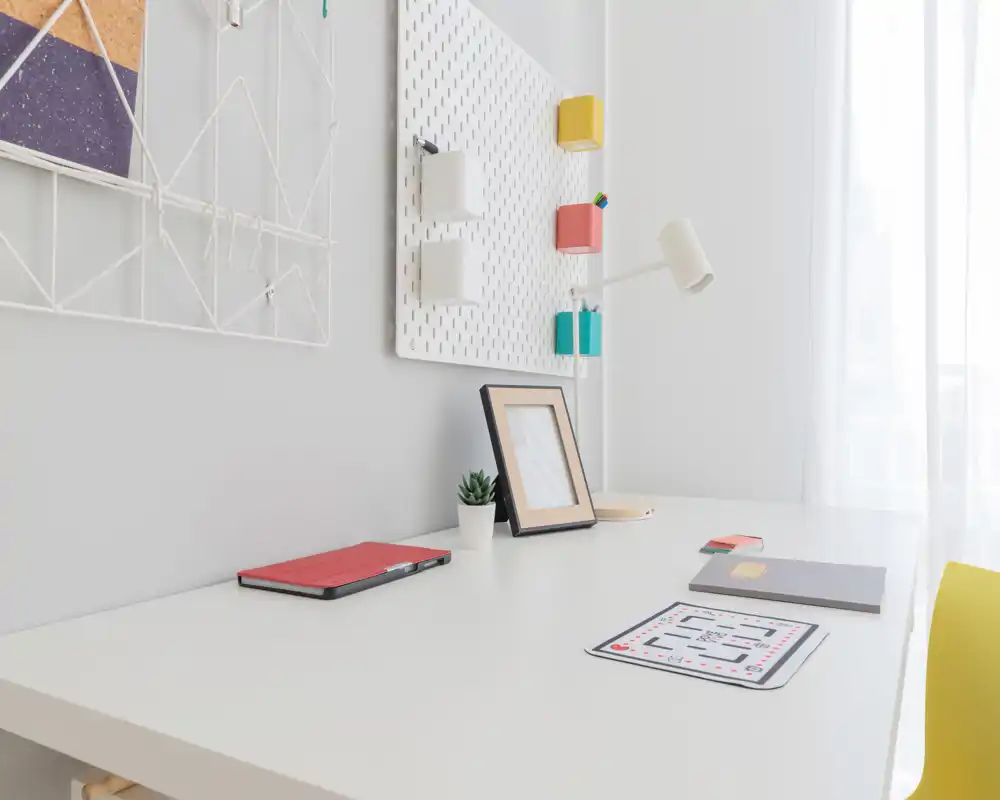 Bright, minimal home workspace with a white desk, task lamp, small plant and colorful wall organizers — ideal for focused work or study.
