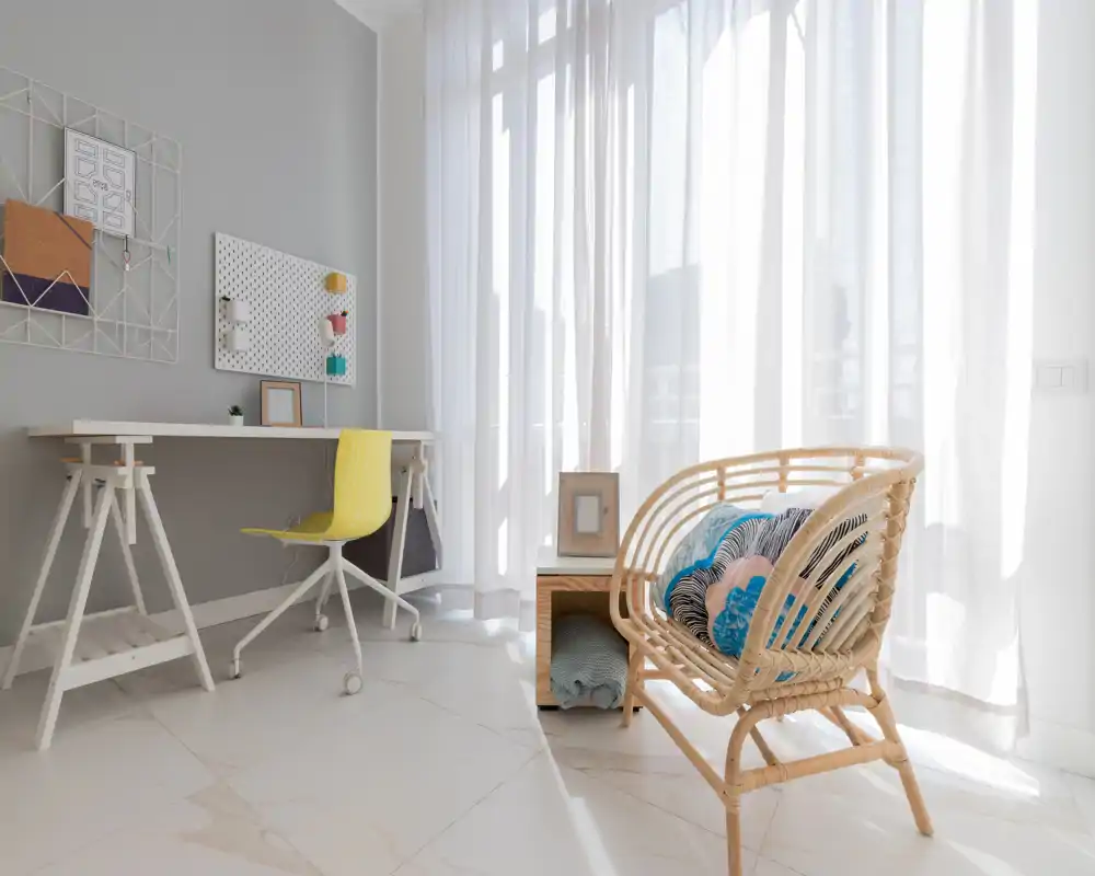 Bright, modern living area with a rattan lounge chair, decorative cushions and a minimalist desk — ideal for relaxing or working in natural light.