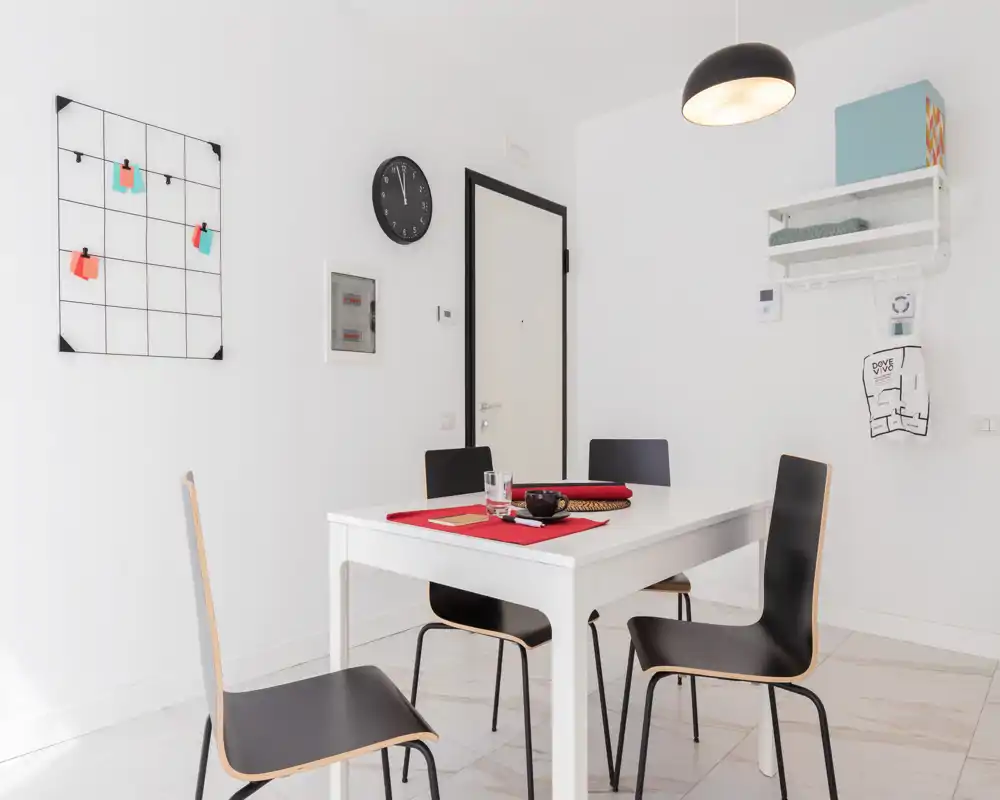 Bright, minimal dining area with a white table and four modern black chairs, simple table setting and clean, airy styling — ideal for listing a compact dining or eat-in space.