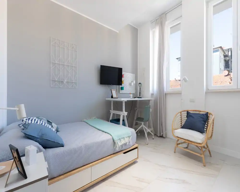 Camera da letto luminosa e moderna con letto completo, tessili accoglienti e una piccola scrivania vicino alla finestra—ideale per soggiorni confortevoli o studio.