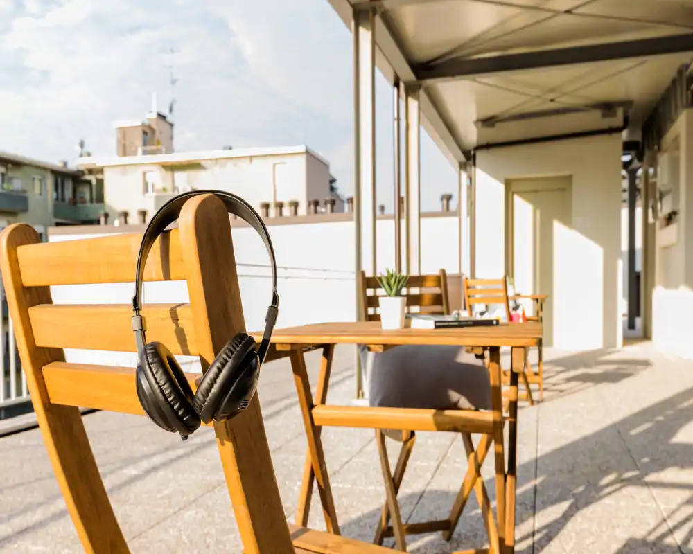 Terrazza soleggiata con sedie e tavolino in legno tipo bistrò, perfetta per colazione o lavoro all'aperto. La luce calda e la vista urbana rendono lo spazio accogliente.