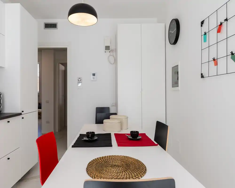 Zona pranzo moderna e minimal con tavolo bianco, sedie colorate e semplici sottopiatti decorativi — luminosa, pulita e adatta a pasti per piccoli gruppi.