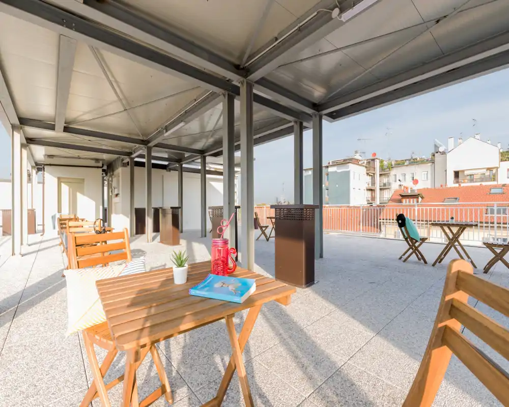 Terrazza panoramica arredata e soleggiata con tavoli e sedie in legno, sedute confortevoli e vista sulla città — perfetta per rilassarsi o pranzare all'aperto.