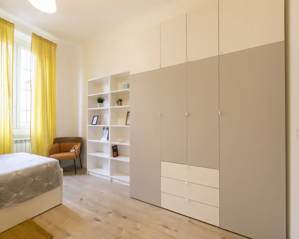 Chambre lumineuse et moderne avec lit confortable, grand placard et fenêtre ensoleillée aux rideaux jaunes qui créent une ambiance chaleureuse.