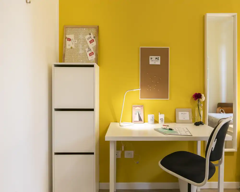 Coin bureau lumineux et chaleureux avec bureau blanc, lampe de travail et rangement sur un mur jaune vif — idéal pour télétravailler ou étudier.