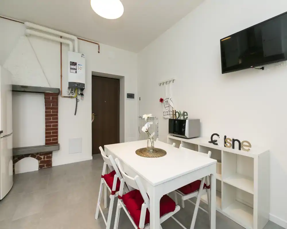 Coin repas lumineux et épuré avec table blanche et quatre chaises aux coussins rouges, étagères minimalistes et TV murale — idéal pour repas décontractés.