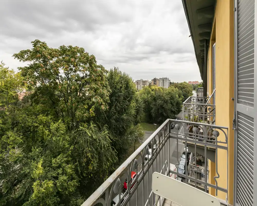 Balcon avec rambarde métallique donnant sur de grands arbres et la ville au loin — idéal pour un café matinal ou se détendre en extérieur.