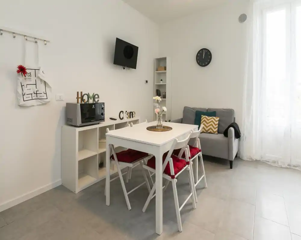 Espace de vie compact et lumineux avec petit canapé, table à manger et chaises — décoration moderne et neutre, lumière naturelle par une grande fenêtre.