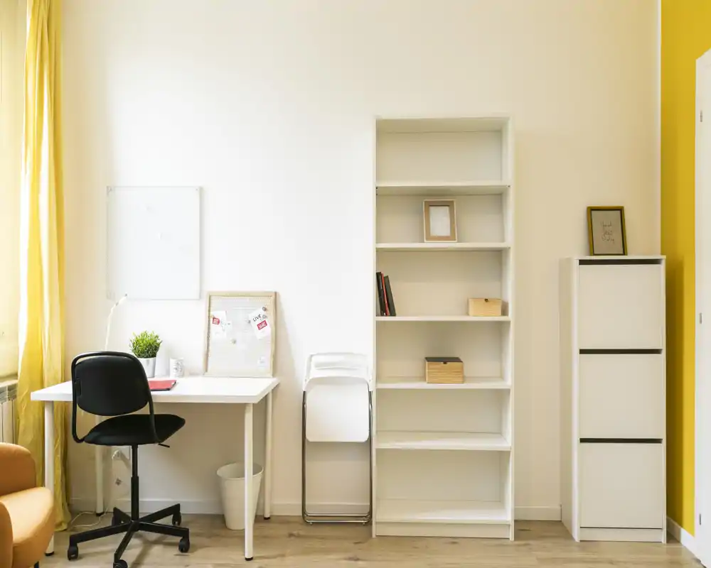Zona de día luminosa y minimalista con escritorio compacto, estanterías y acentos amarillos cálidos — ideal para teletrabajo o estudio.