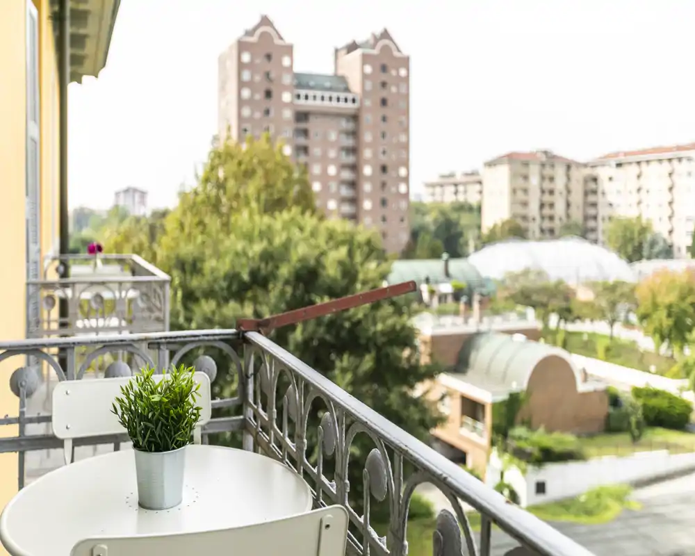 Sunny balcony with a small table, two chairs and a potted plant overlooking a residential neighborhood — ideal for morning coffee.
