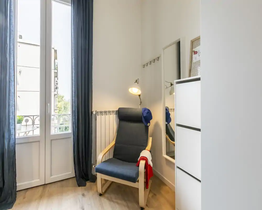 A bright, cozy corner with a comfortable armchair, floor lamp and tall window/door letting in abundant natural light — ideal for reading or relaxing.