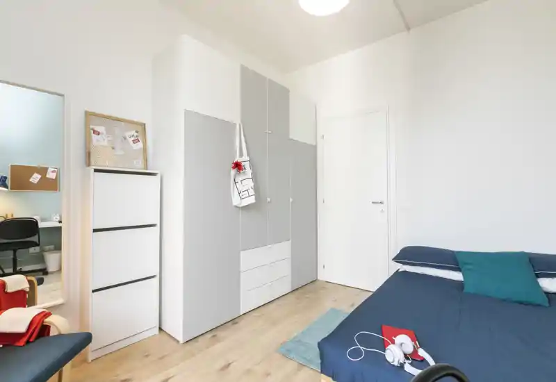 Camera da letto luminosa e moderna con letto matrimoniale ben rifatto, un ampio armadio grigio e pavimento in legno chiaro — stile minimal pulito e buona luce naturale.