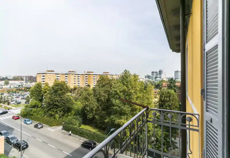 Balcón soleado con vistas a una calle arbolada y bloques de apartamentos cercanos; ideal para tomar café por la mañana con vistas a la ciudad.