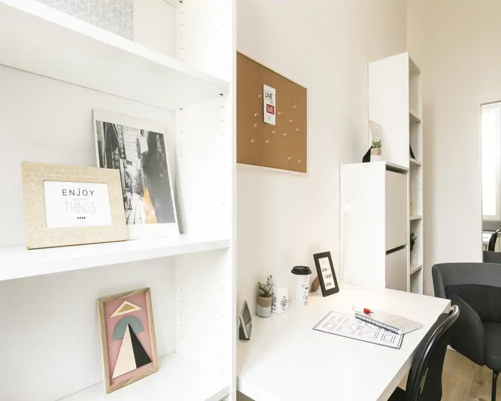 Espacio de oficina en casa / sala luminoso y minimalista con escritorio blanco, estanterías, marcos decorativos y un sillón cómodo, ideal para trabajar.
