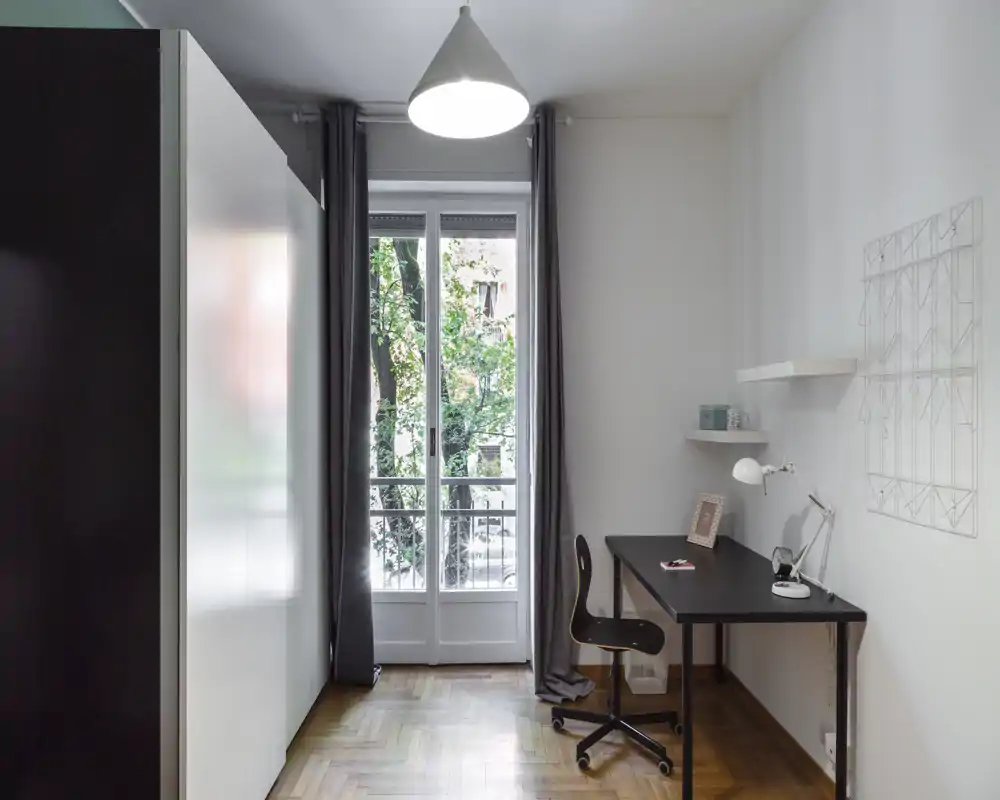 Minimalist bedroom corner with large wardrobe and a workspace by a bright balcony door; clean lines, wood floor and neutral decor make it suitable for a calm rental listing.