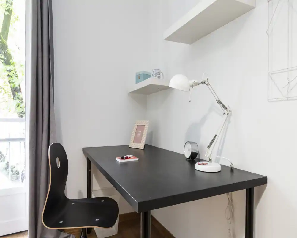 Minimal, bright workspace corner with a black desk, task lamp and chair next to a window — ideal to highlight a study area in the listing.