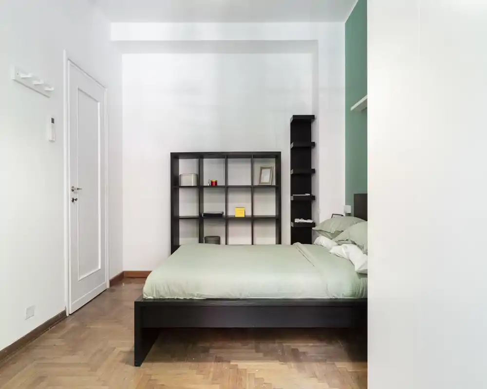Bright, modern bedroom with a low dark wooden bedframe, mint-green bedding and a minimalist shelving unit; clean lines and natural light create a calm atmosphere ideal for rental listings.