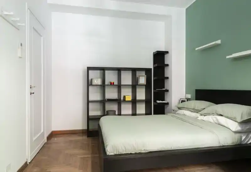 Bright, modern bedroom with a neatly made double bed, mint-green bedding and minimalist shelving — calm, well-lit space ideal for restful stays.