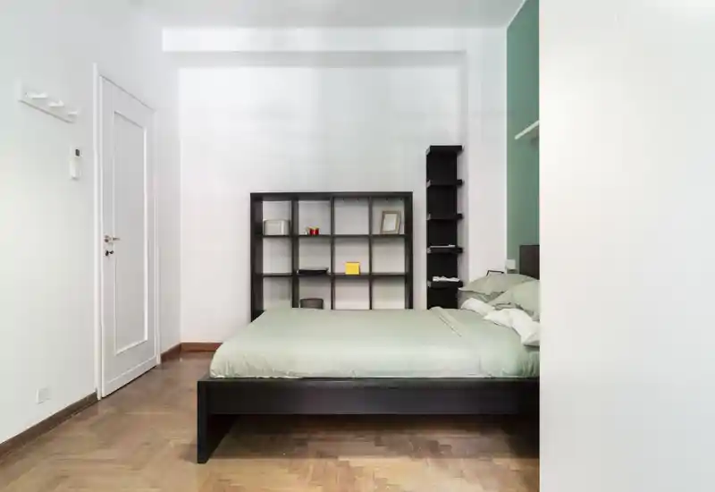 Bright, modern bedroom with a low dark wooden bedframe, mint-green bedding and a minimalist shelving unit; clean lines and natural light create a calm atmosphere ideal for rental listings.