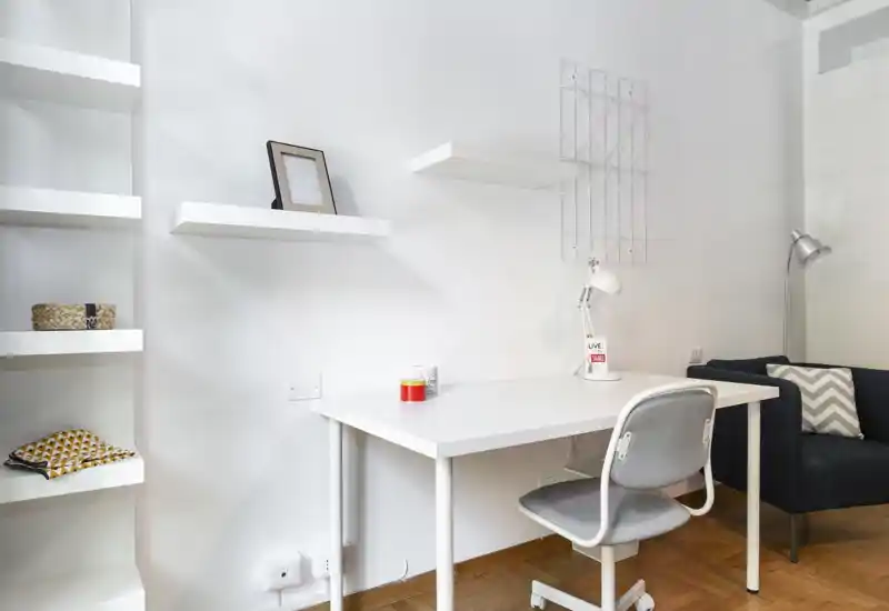 Bright, minimal living area with a white desk, shelving and a compact sofa — ideal for working from home or relaxing in a small apartment.