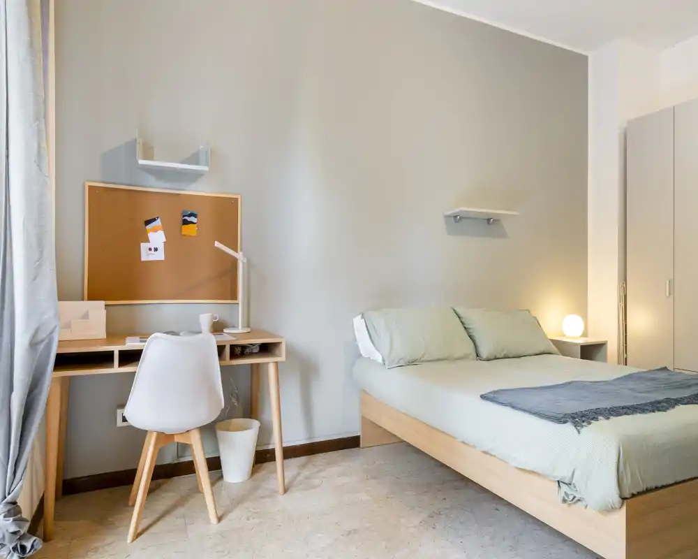 Bright, neatly staged bedroom with a double bed, bedside lamp and a small desk — ideal for short stays or business travel.