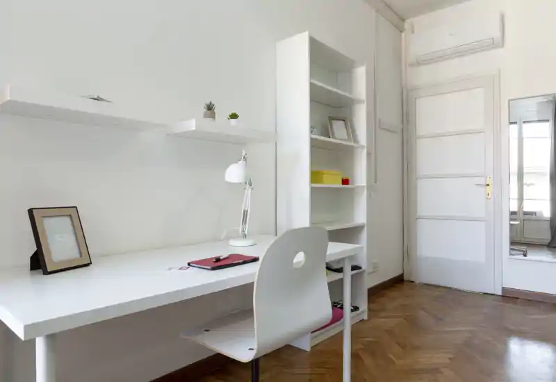 Angolo studio luminoso e minimal con scrivania bianca, sedia, scaffalatura e pavimento in parquet — spazio di lavoro pulito e moderno ideale per lo studio o il lavoro da remoto.