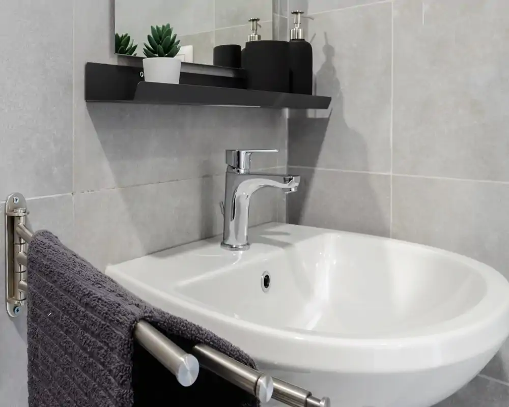 Lavabo moderno e pulito con rubinetto cromato, pareti piastrellate grigie e asciugamano su un supporto in acciaio—dettaglio perfetto per gli annunci.