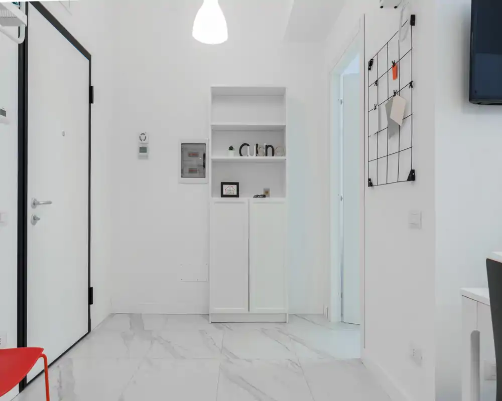 Ingresso luminoso e minimalista con pareti bianche, pavimento effetto marmo e un modulo contenitore sottile; lampada a sospensione moderna e arredo ordinato rendono l'ingresso accogliente.