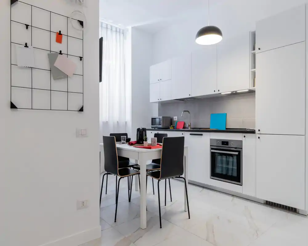 Cucina moderna e luminosa con pensili bianchi, forno incorporato e un piccolo tavolo da pranzo per quattro persone — ben illuminata e ordinata, ideale per un appartamento compatto.