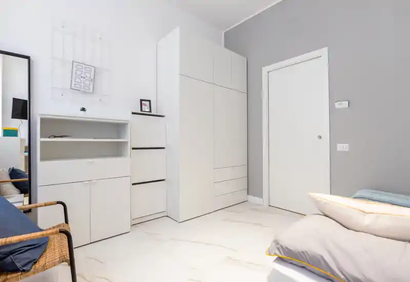 Angolo di camera da letto luminoso e moderno con un angolo del letto visibile, armadi bianchi e ripostiglio minimalista — design pulito e toni neutri.