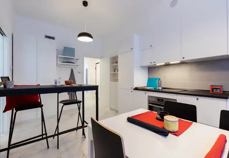 Modern fitted kitchen with white cabinets, integrated oven and a small dining area; bright, clean and stylishly staged for rental photos.