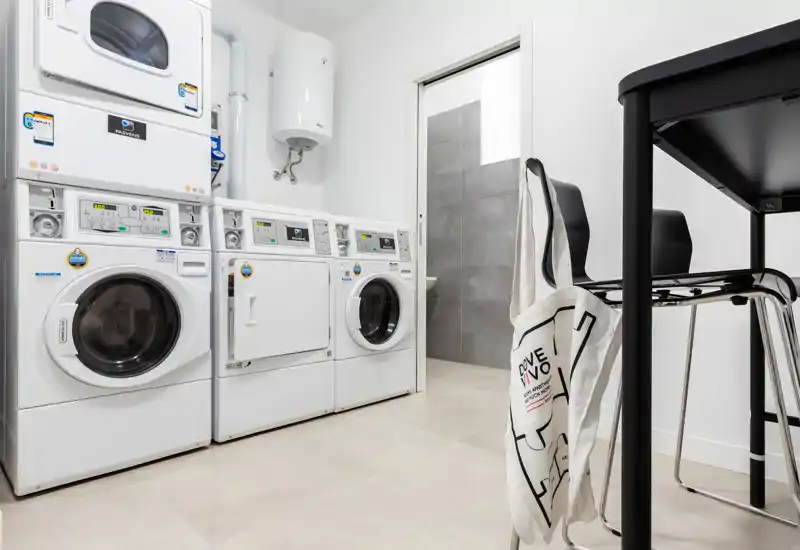Clean, modern laundry/utility room with multiple front-load washers and a stacked dryer; bright white walls and tiled floor create a functional, well-lit space.