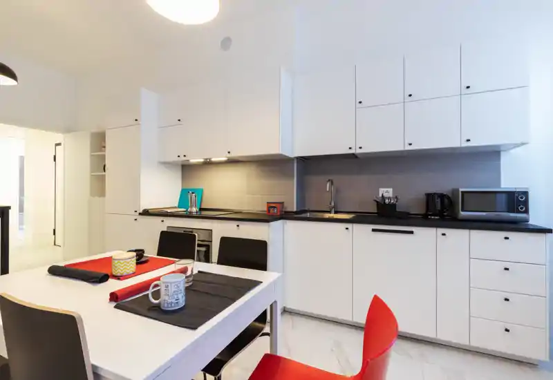 Modern fitted kitchen with white cabinets, black countertop and a dining table set for four; bright, clean and practical layout ideal for short-term rentals.