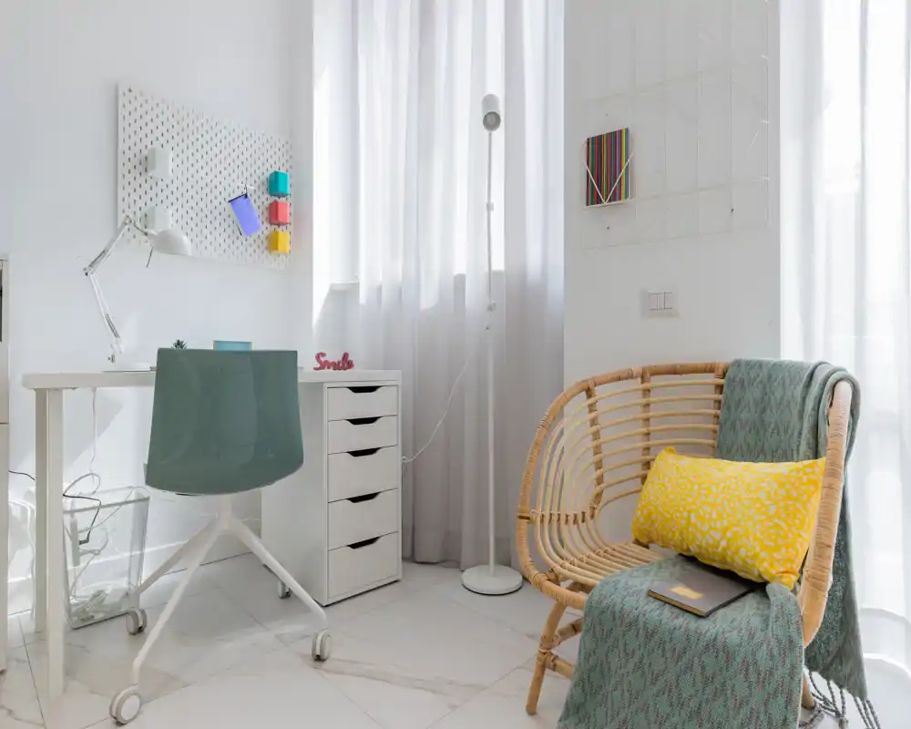 Bright, modern sitting corner with a rattan armchair, soft textiles and a small desk — ideal for relaxing or light work in a cozy living area.