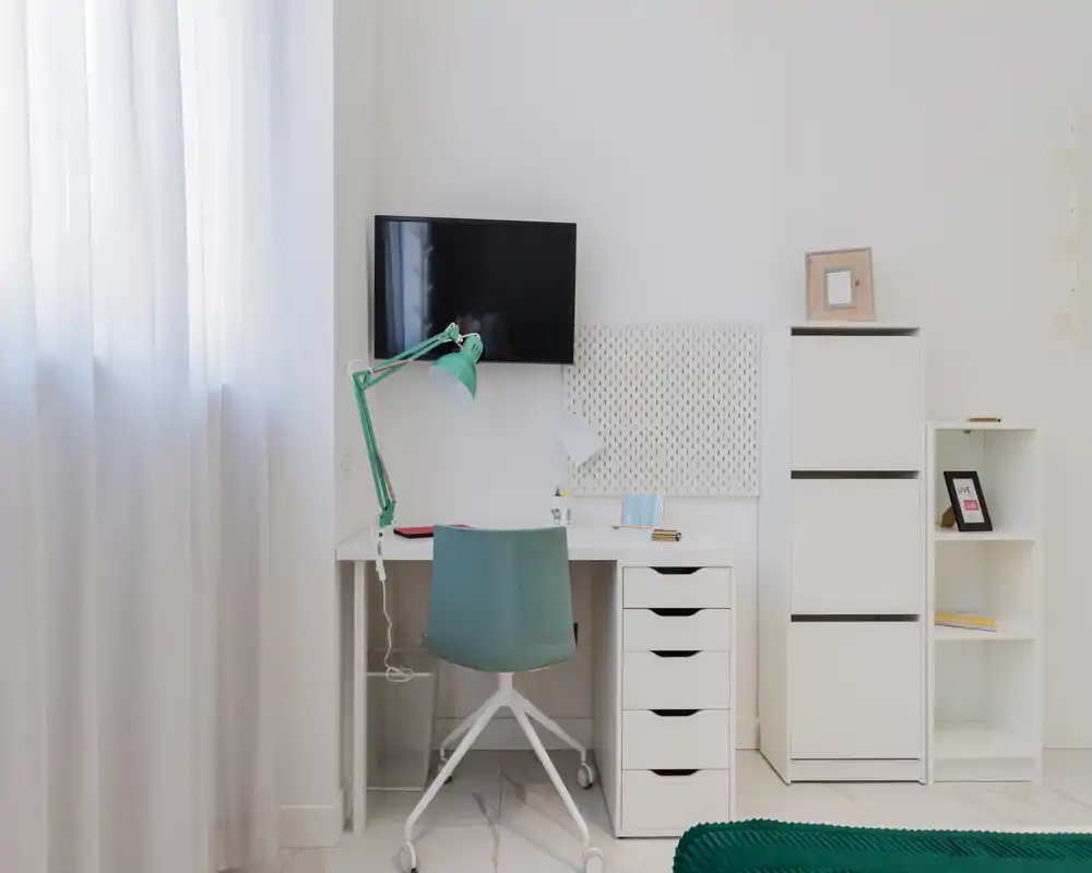 Coin bureau lumineux et minimal près de la fenêtre — bureau blanc avec tiroirs, chaise et lampe turquoise pour un coin home office épuré avec rangements.