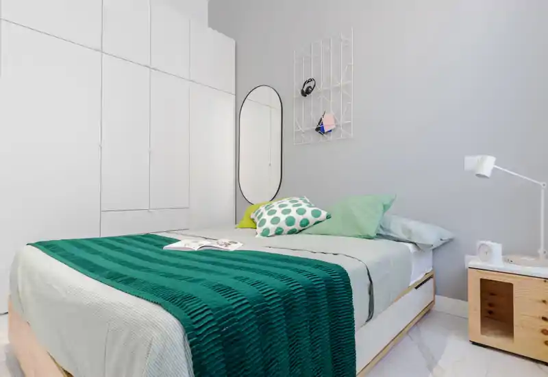 Chambre moderne et lumineuse avec lit double bien fait, jeté vert et coussins décoratifs, grand placard intégré et table de chevet avec lampe — idéale pour une annonce mettant en avant confort et rangements.