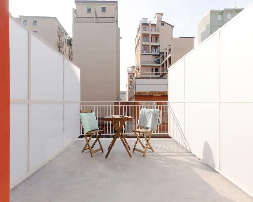 Terrasse privée ensoleillée avec une petite table en bois et deux chaises pliantes, idéale pour le café du matin ou un verre en soirée. Panneaux d'intimité et vue urbaine pour un espace abrité.