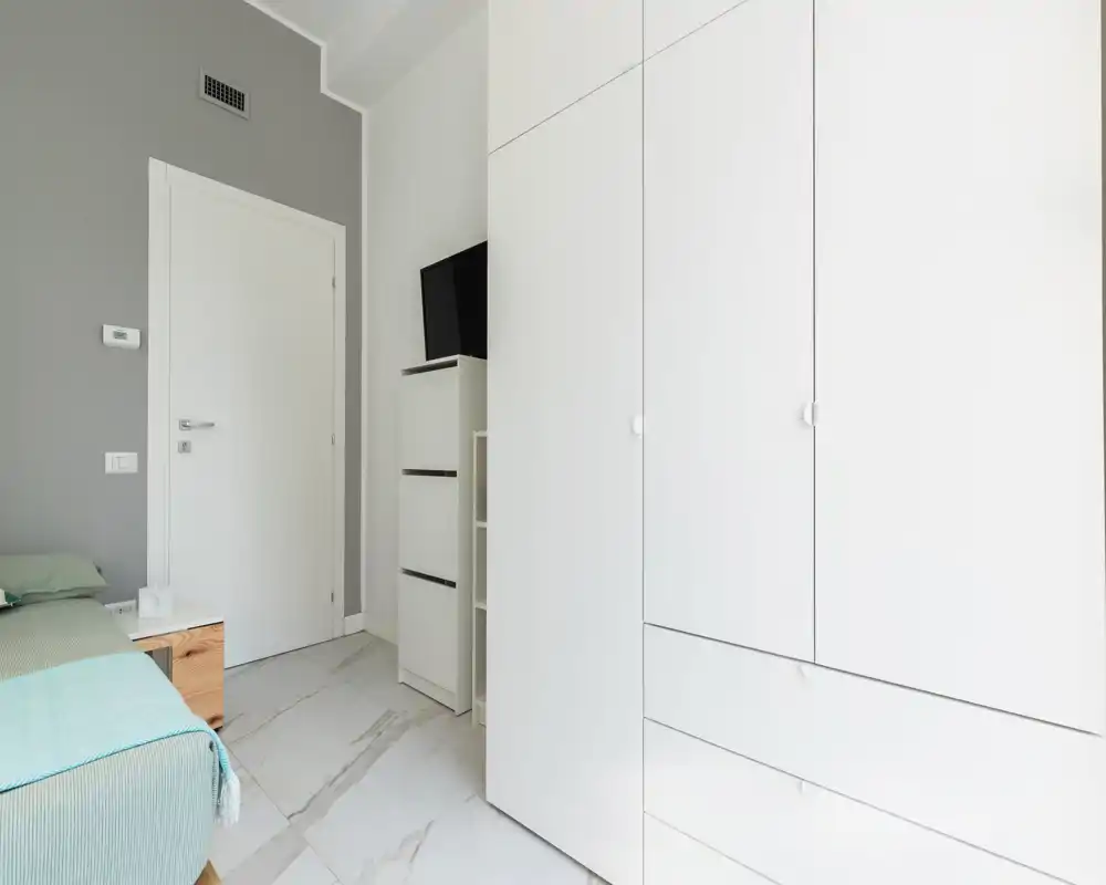 Coin de chambre lumineux et moderne avec lit partiellement visible, table de chevet et grand placard blanc ; décoration minimaliste et lignes épurées pour une ambiance apaisante.