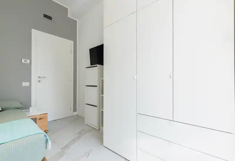 Coin de chambre lumineux et moderne avec lit partiellement visible, table de chevet et grand placard blanc ; décoration minimaliste et lignes épurées pour une ambiance apaisante.