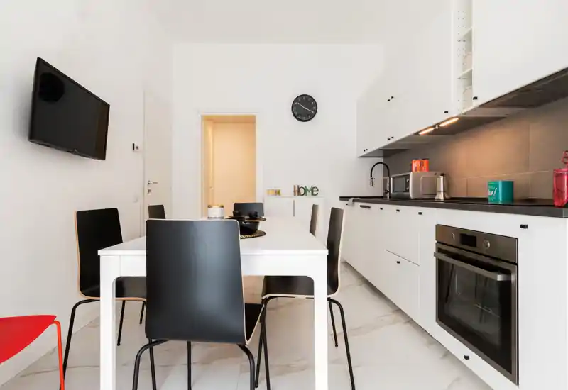 Bright modern kitchen with integrated white cabinetry, black countertop and a dining table with black chairs — a clean, functional space ideal for meals and cooking.