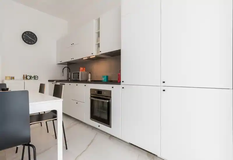 Bright modern kitchen with white cabinetry, integrated oven and minimalist dining area — clean lines and practical appliances ideal for a rental.