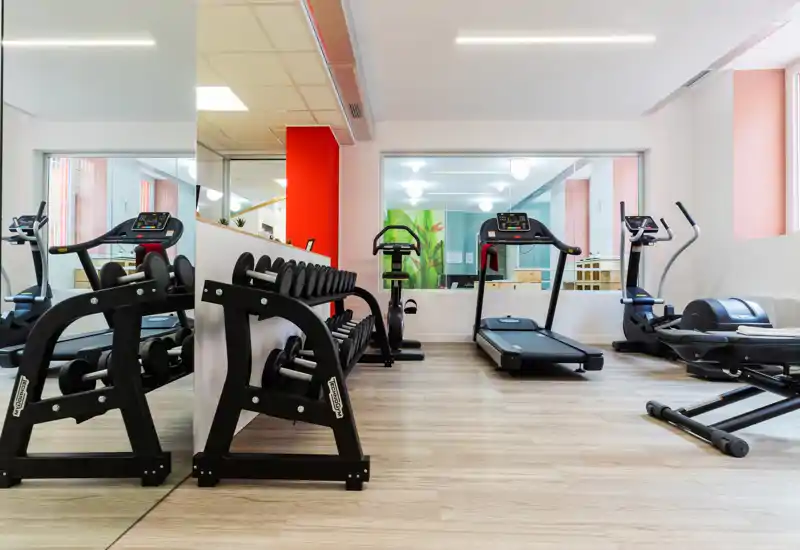 Small fitness room with treadmills, elliptical machines and a rack of dumbbells, mirrored wall and bright, modern finishes.