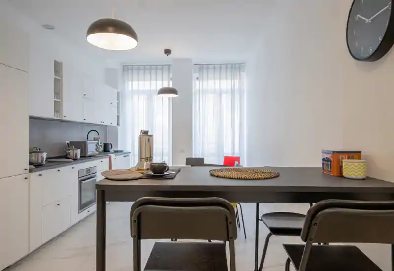Bright modern kitchen with a central breakfast bar, white cabinetry, built-in oven and tall windows that flood the space with natural light.