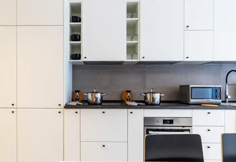 Modern white kitchen with integrated cabinetry, stovetop, oven and microwave on a dark countertop; neatly arranged pots and accessories create a clean, inviting cooking space.