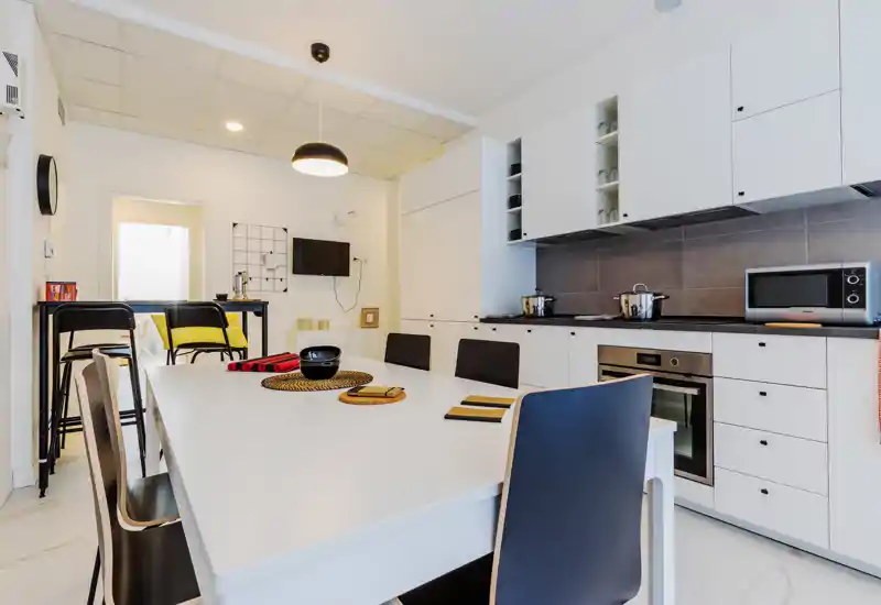 Bright modern kitchen with a large white dining table, built-in oven, microwave and upper cabinets; neat styling and seating for several guests.