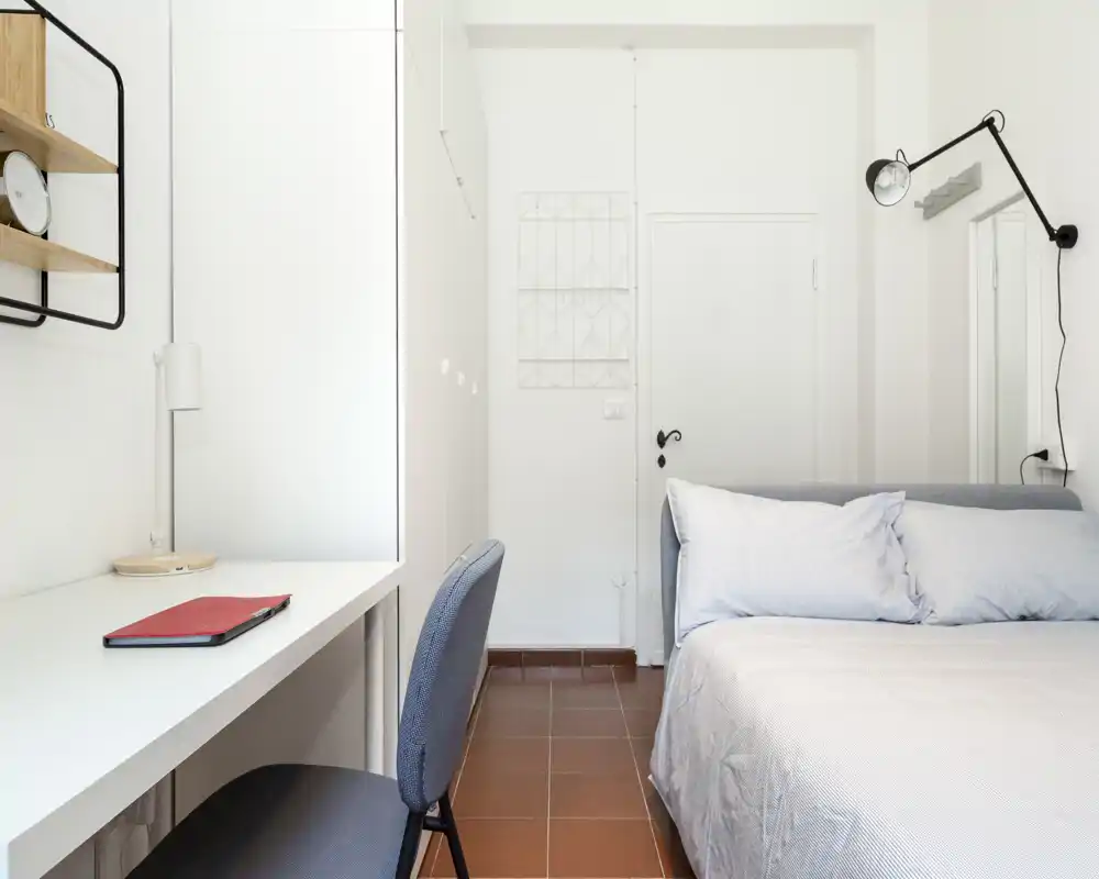 Dormitorio luminoso y minimalista con cama doble cómoda, almohadas suaves y un escritorio de estudio, ideal para una persona o pareja que busque un espacio funcional.