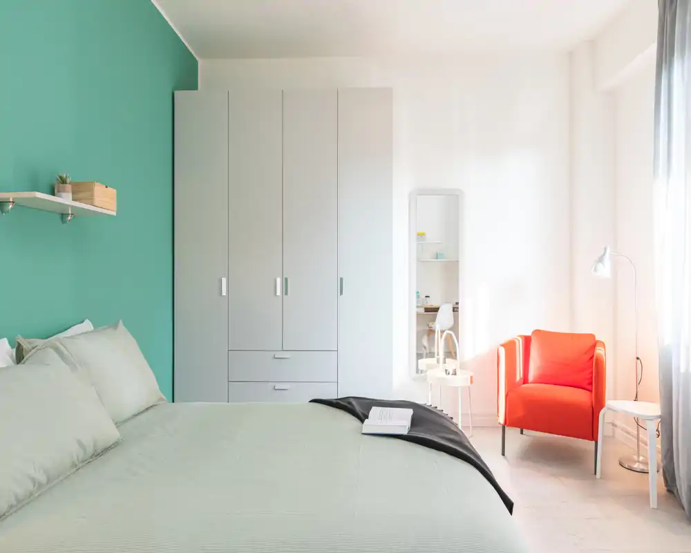 Bright, modern bedroom with a well-made double bed, large wardrobe and a comfy red accent armchair by the window — ideal for rental photos showcasing calm, stylish sleeping quarters.