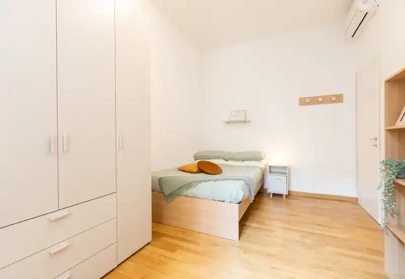 Camera da letto luminosa e minimalista con letto matrimoniale su base in legno chiaro, biancheria verde tenue e pavimenti caldi in legno — spazio pulito e accogliente ideale per il riposo.