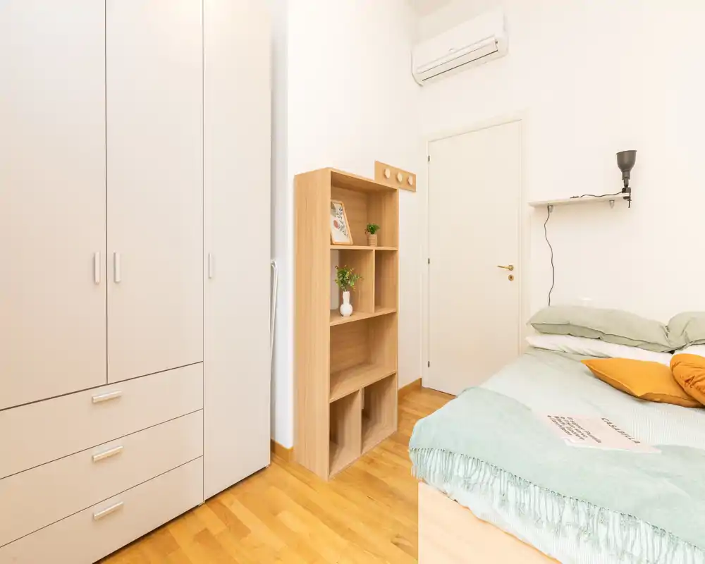 Camera da letto luminosa e minimal con letto ben rifatto, armadio e scaffale aperto — stile moderno e pulito, ideale per annunci di affitto.