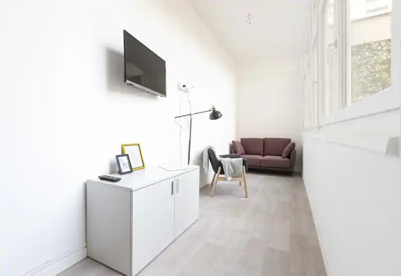 Zona giorno luminosa e minimale con divano compatto, poltrona e TV a parete: grandi finestre illuminano l'ambiente rendendolo moderno e tranquillo.